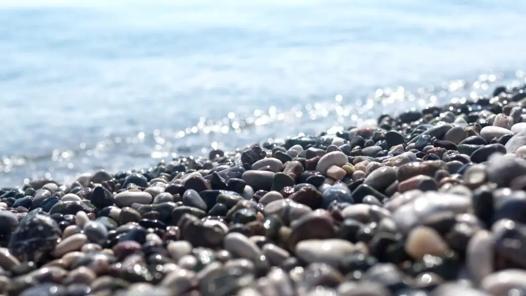 A pebble beach with light blue water behind it. This image is for Avery Thatcher's public speaking and live workshops for corporations and non-profits to help their team navigate chaotic times, burnout, stop feeling out of control and improve their company culture.